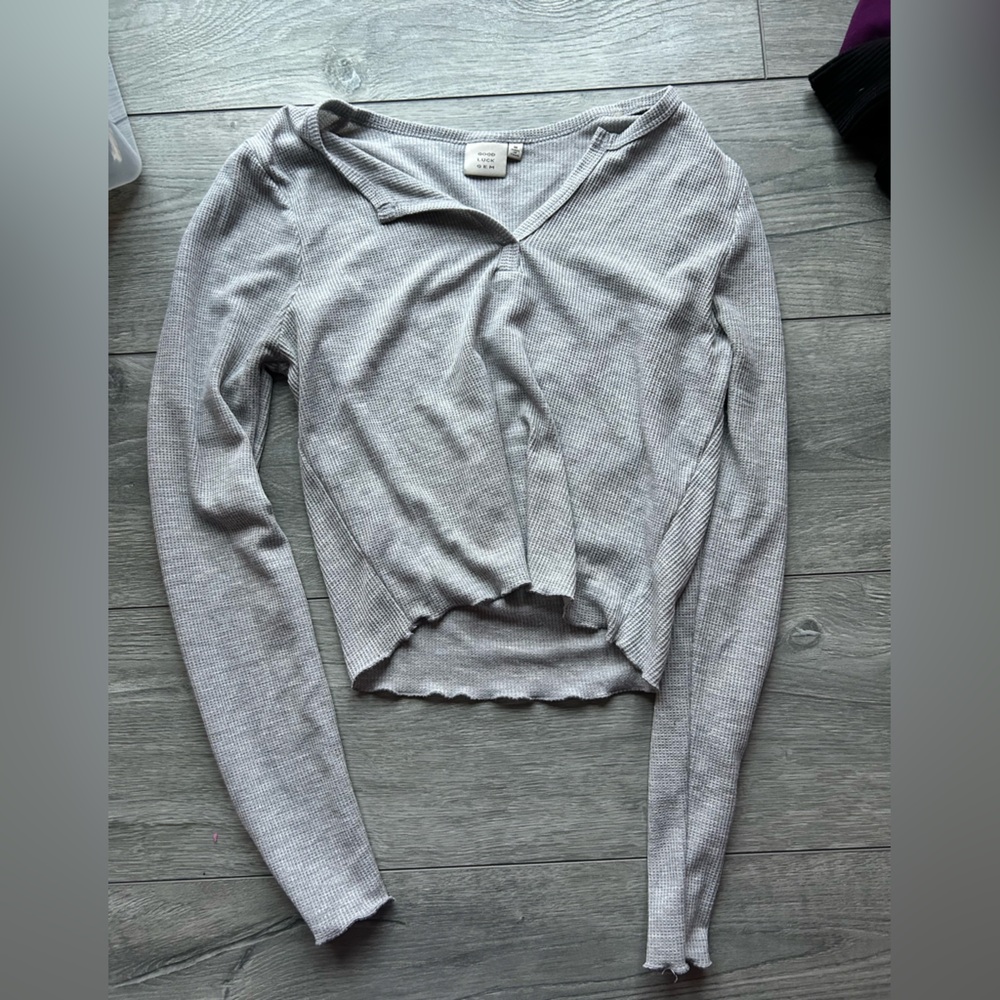 Woman’s gray long sleeve top with ruffle hem on bottom and on ends of sleeves.
